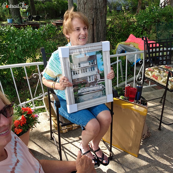Picture of a woman holding birthday portraits that show a white house surrounded by trees