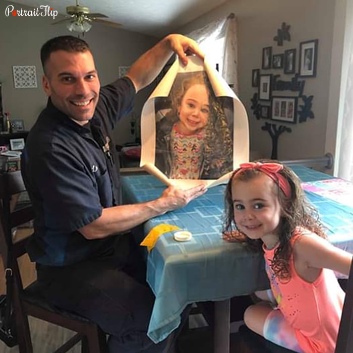 Picture of a man holding child portraits that include a young girl who is sitting next to the man