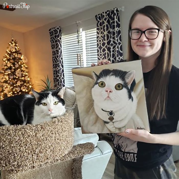 Picture of a woman holding Christmas portraits that include her cat, along with her cat sitting next to her on the couch