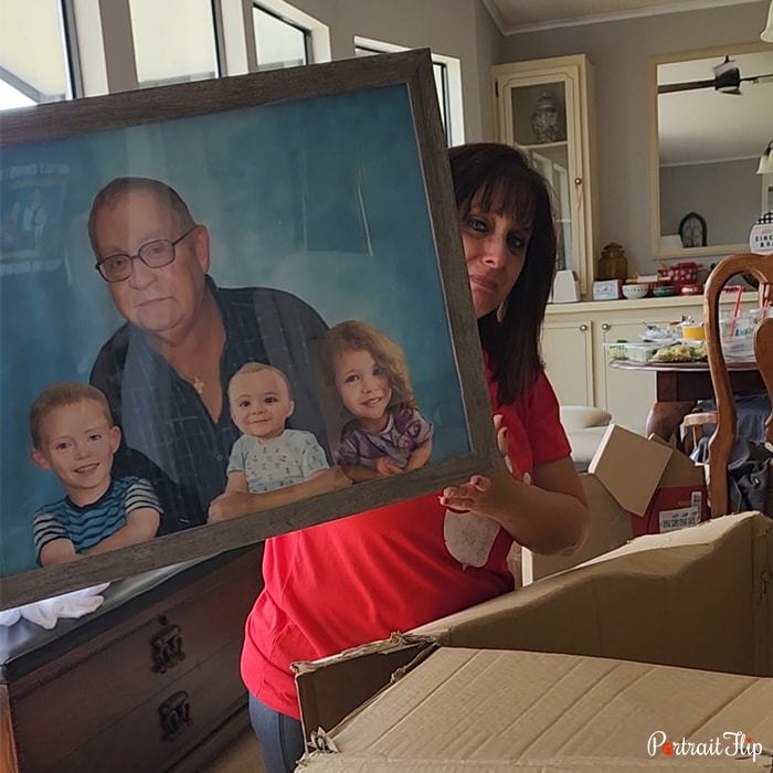 Picture of a woman peeking from behind the memorial portraits which she holds that show an old man with three children, one boy, a girl, and a baby