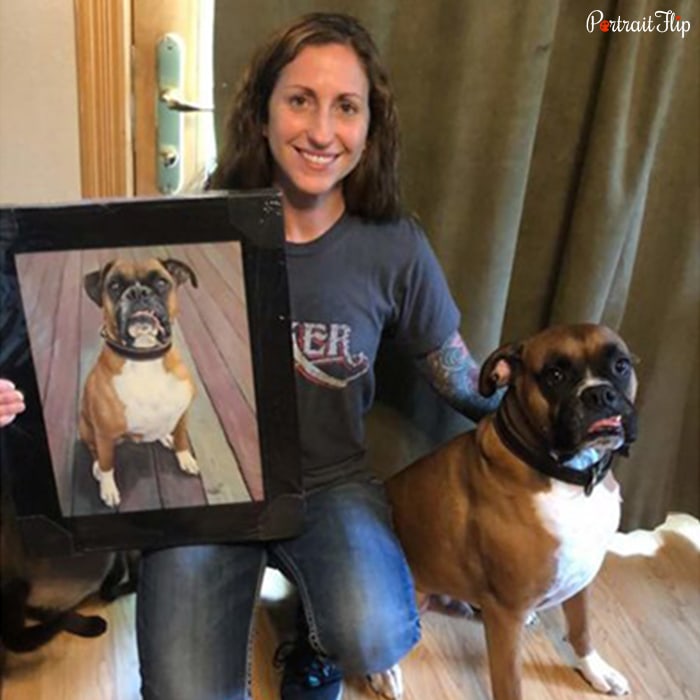 Picture of a woman holding mother’s day paintings, which include her dog, who is also sitting beside her